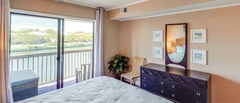 A bedroom with a large bed, a dresser, a chair, and a balcony with a view of the outdoors.