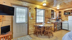 Interior de una cabaña de madera con comedor, cocina y televisor montado en la pared.