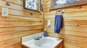 A wooden-paneled bathroom with a white sink, a mirror, a towel rack, and a hand soap dispenser.