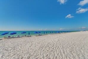 A beach with white sand, blue umbrellas, and lounge chairs. - Sunset-view Resort Condo on Perdido Key (Pensacola)