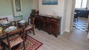A dining area with a wooden table set for four, a dark wooden cabinet, and a painting of a coastal scene. - Chapel Hill House (Pembroke)