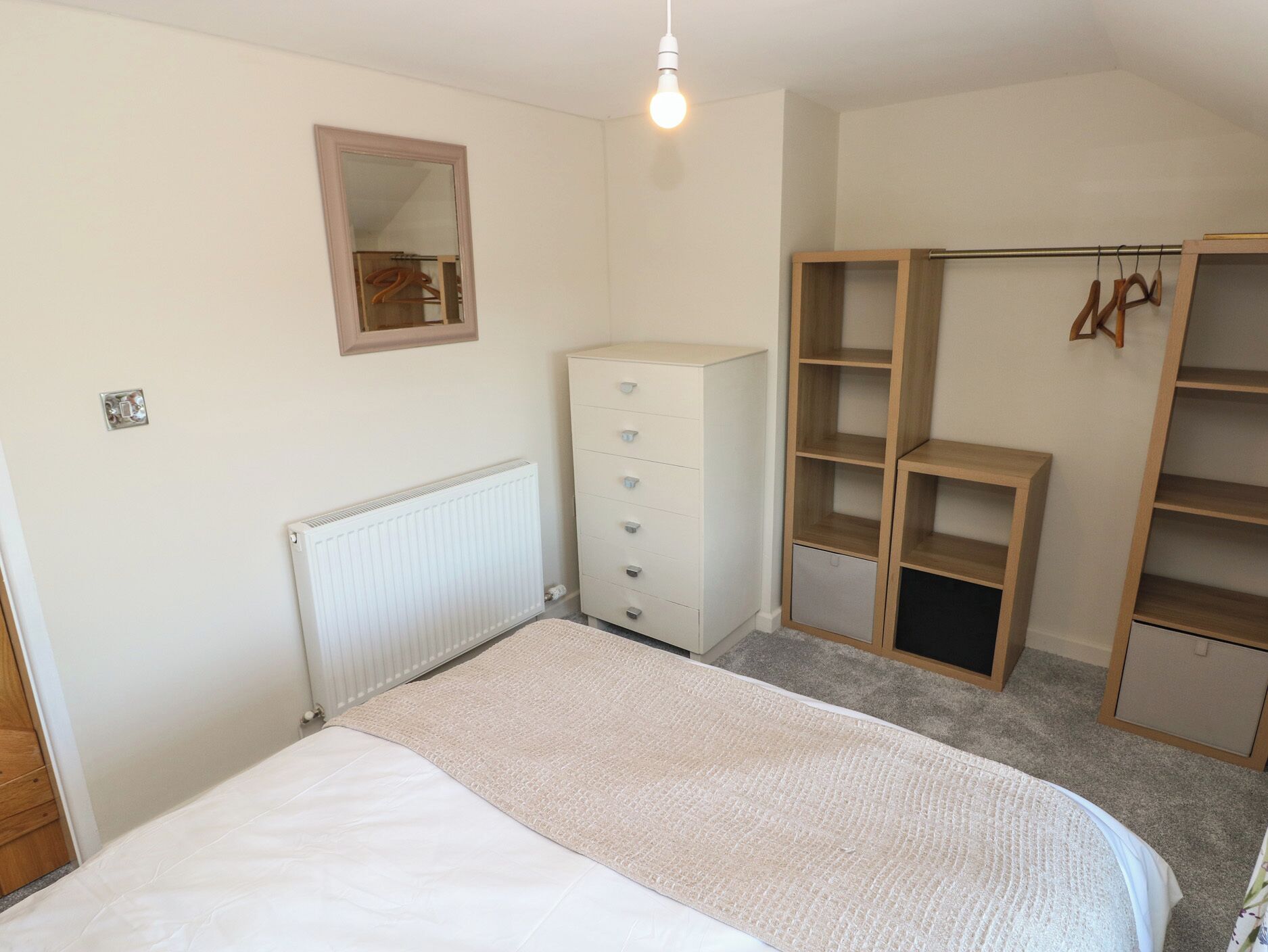 A bedroom with a bed, a dresser, a radiator, a wardrobe, and a hanging rack.