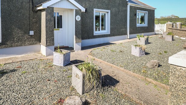A two-story house with a white door and windows, surrounded by gravel and potted plants. - Chapel Hill House (Pembroke)