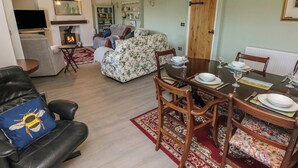 A living room with a fireplace, a sofa, a dining table set for four, and a television in the corner. - Chapel Hill House (Pembroke)