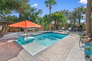 A rectangular swimming pool with a tiled deck, surrounded by palm trees and lounge chairs.