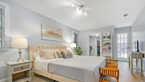 Um quarto com cama, mesas de cabeceira, uma cadeira, escrivaninha e estante de livros.