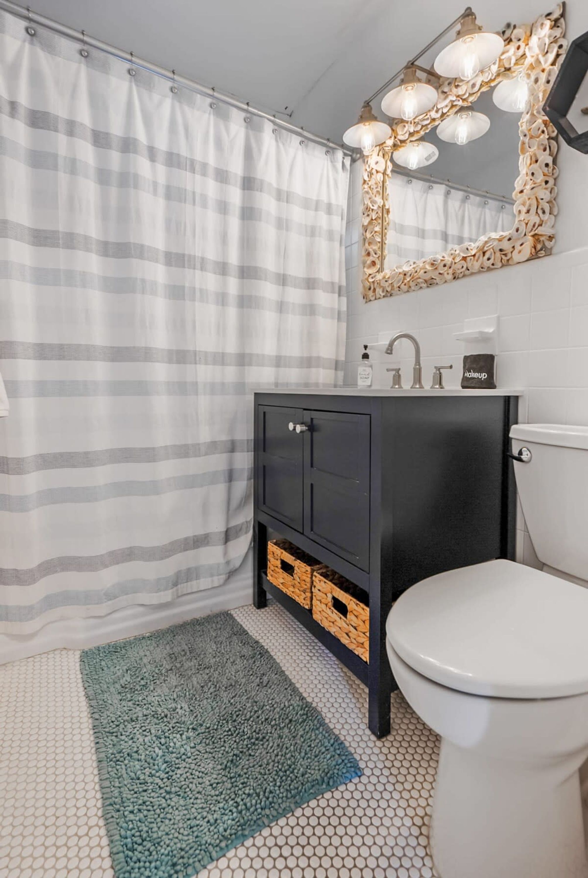A bathroom with a striped shower curtain, a black vanity with a mirror, a white toilet, and a green rug.