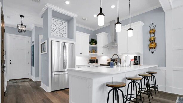 A modern kitchen with white cabinetry, a central island with stools, stainless steel appliances, and pendant lighting. - Downtown St Augustine Steps to Ice Plant Upscale (St. Augustine)