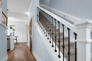 Un escalier avec des balustrades noires et des rampes blanches, menant à un palier où se trouvent une porte et une petite table.