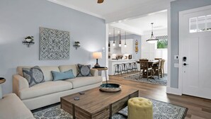 A modern living room with a sofa, coffee table, and a dining area with a table and chairs. There is a kitchen in the background with bar stools. - Downtown St Augustine Steps to Ice Plant Upscale (St. Augustine)