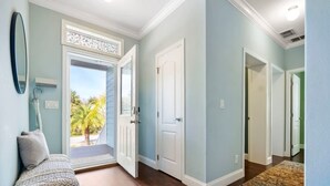 Un couloir avec un banc, une porte et une vue sur des palmiers à l’extérieur.
