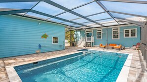 Une piscine avec un patio couvert, une maison bleue et du mobilier d’extérieur.