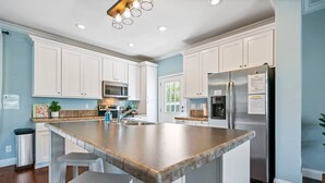 Une cuisine moderne avec des meubles blancs, un grand îlot central doté de tabourets, des appareils électroménagers en acier inoxydable et un mur de couleur bleu clair.