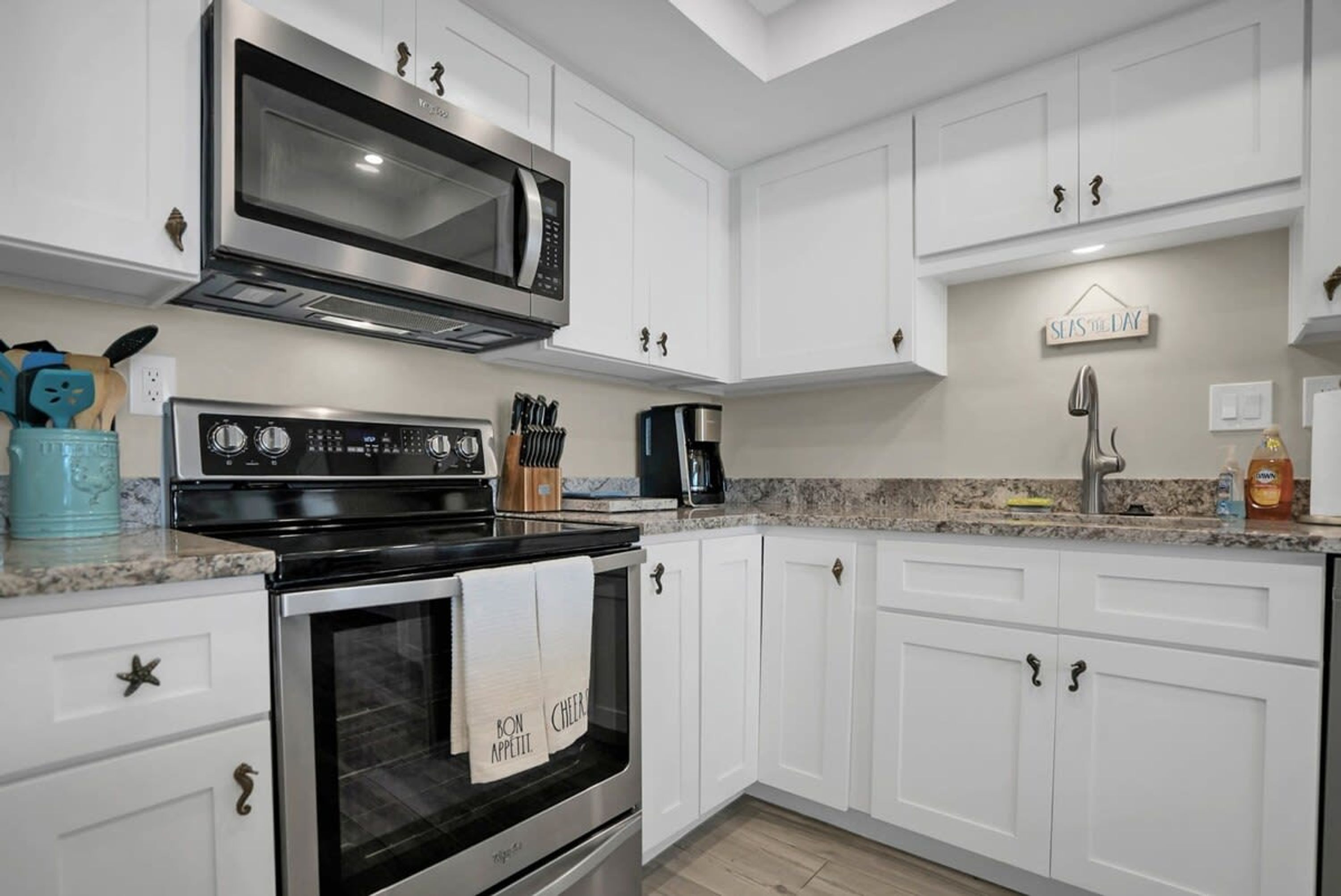 A modern kitchen with white cabinets, a stainless steel stove, a microwave, and a coffee maker.