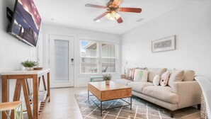 A modern living room with a sofa, coffee table, and TV. - 100 Steps to Sand Free Parking Smart TV Patio (St. Augustine)