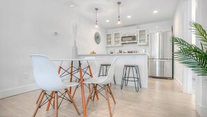 A modern kitchen with white cabinetry, stainless steel appliances, and a central island with stools. - 100 Steps to Sand Free Parking Smart TV Patio (St. Augustine)
