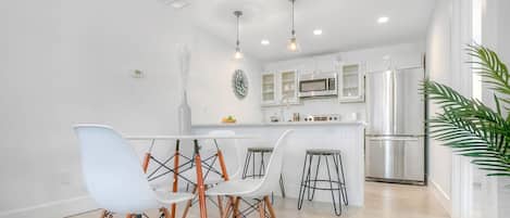 Uma cozinha moderna com armários brancos, eletrodomésticos de aço inoxidável e uma ilha central com banquetas.
