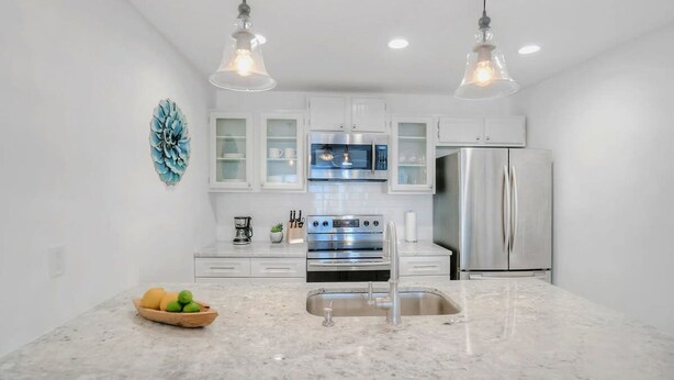 A modern kitchen with white cabinets, stainless steel appliances, and a marble countertop. - 100 Steps to Sand Free Parking Smart TV Patio (St. Augustine)