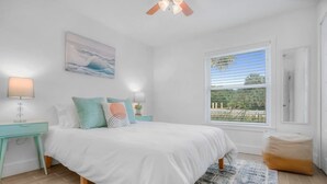 A bedroom with a bed, nightstands, a window with a view, and a ceiling fan. - 100 Steps to Sand Free Parking Smart TV Patio (St. Augustine)