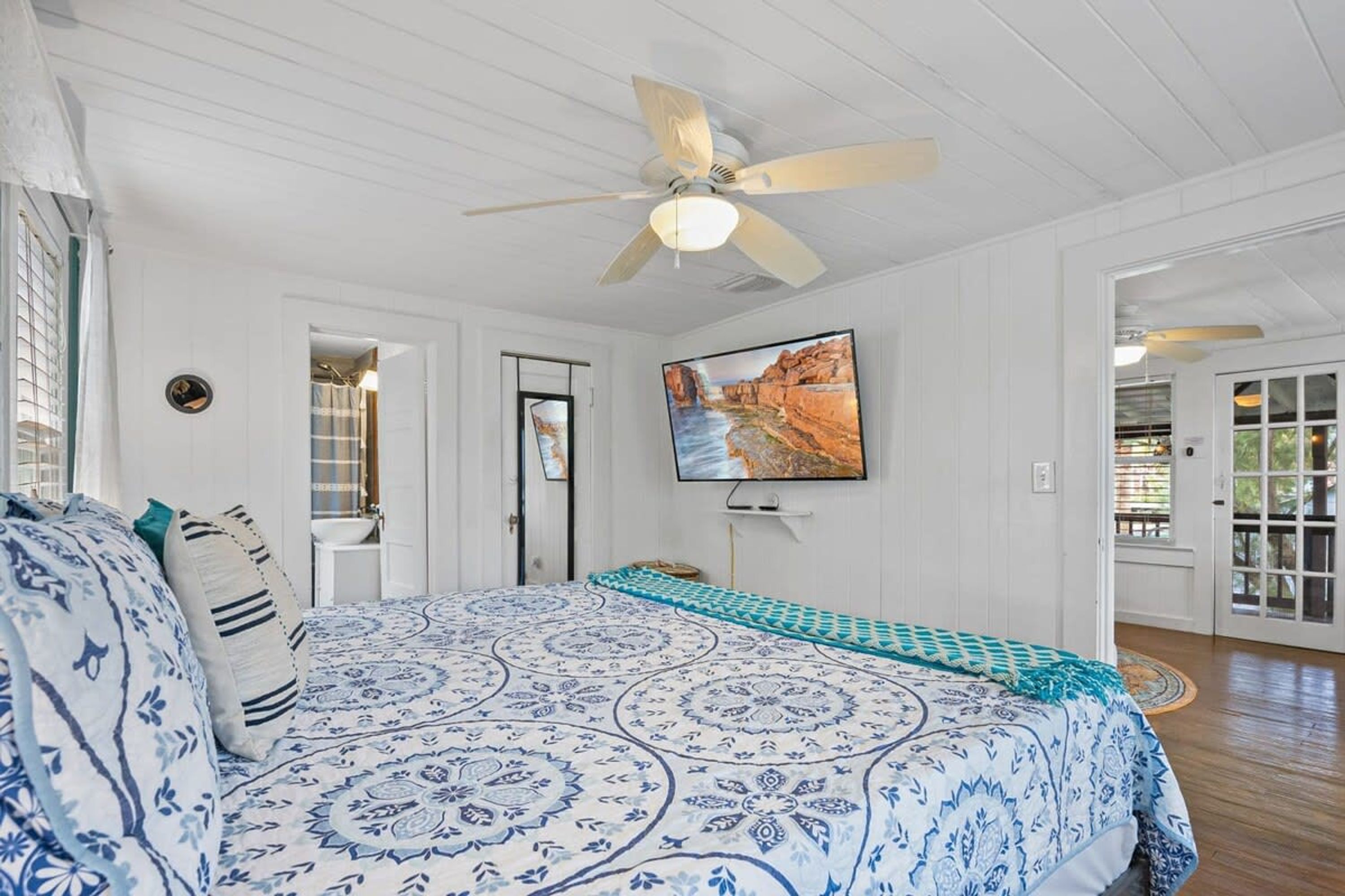 A bedroom with a bed, a ceiling fan, a TV, and a door leading to another room.