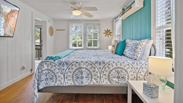 A bedroom with a bed, a ceiling fan, a window with blinds, and a wall-mounted clock. - Marvelous Mermaid Beach Bungalow Dog-friendly (St. Augustine)