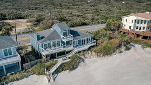 Een huis aan de kust met een balkon, een trap naar de hoofdingang en een zandstrand in de buurt.