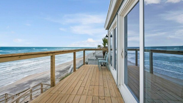 Een houten terras met een glazen deur die uitkomt op een balkon met uitzicht op de oceaan.