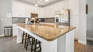 A kitchen with white cabinets, a granite countertop, stainless steel appliances, and a central island with stools.