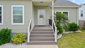 A two-story house with a front porch, a front door, and a small garden area with plants and a palm tree.