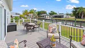 A deck with outdoor furniture, a grill, and a view of a residential area with houses and a fence.