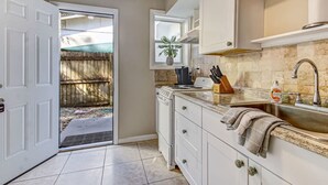 A kitchen with white cabinets, a granite countertop, a sink, and a window with a plant. - Free Parking Smart TV Uptown St Augustine (St. Augustine)