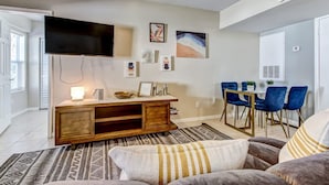 A modern living room with a flat-screen TV, wooden entertainment unit, and a dining area with blue chairs. - Free Parking Smart TV Uptown St Augustine (St. Augustine)