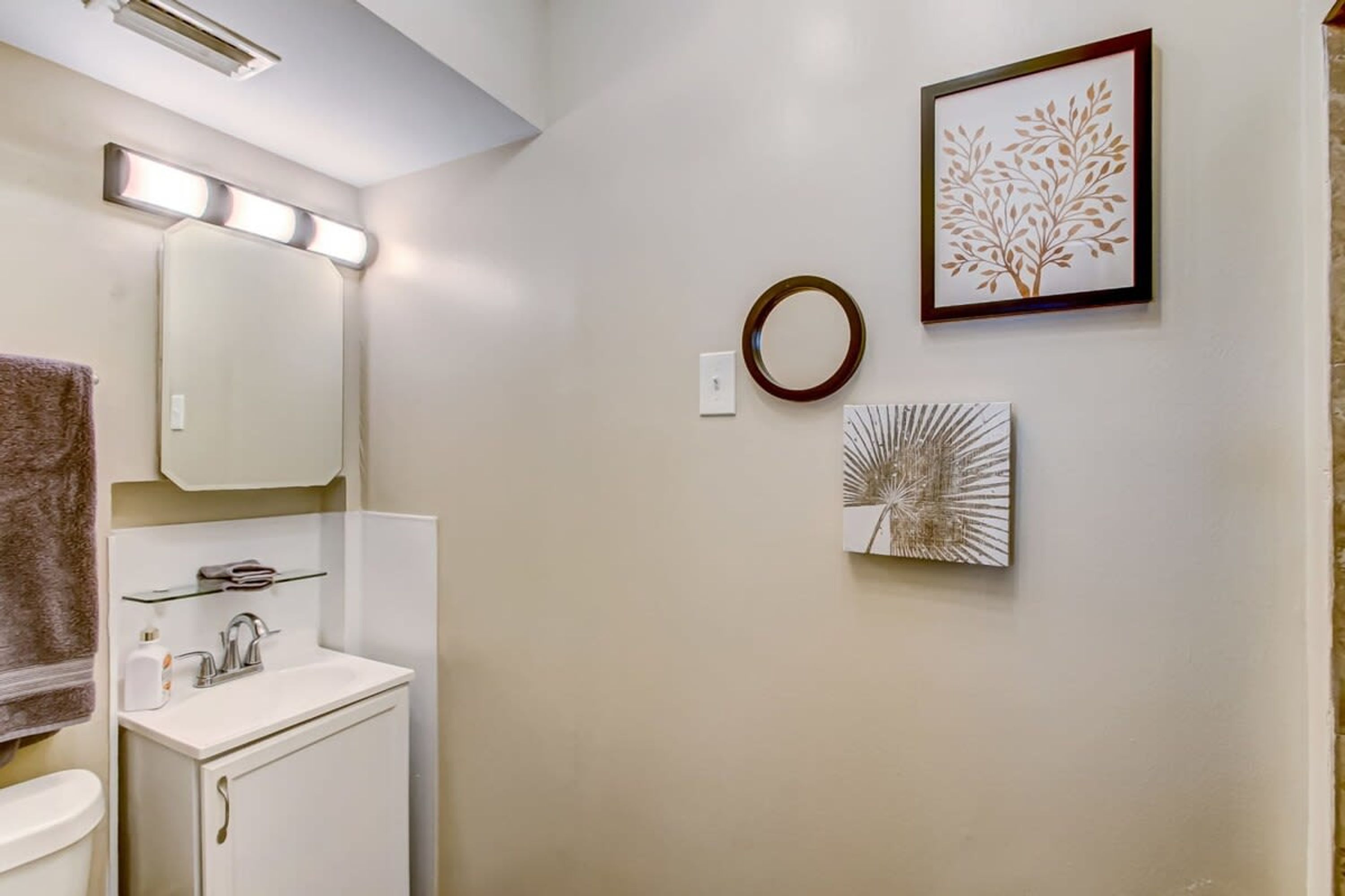 A bathroom with a white sink, a mirror, and a towel rack. There are wall-mounted lights and two framed artworks.