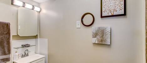 A bathroom with a white sink, a mirror, and a towel rack. There are wall-mounted lights and two framed artworks.