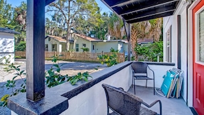 A covered patio with two wicker chairs, a red door, and a view of neighboring houses. - Free Parking Smart TV Uptown St Augustine (St. Augustine)