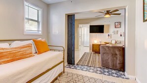 A bedroom with a bed, a ceiling fan, a window with blinds, and a view into the living area. - Free Parking Smart TV Uptown St Augustine (St. Augustine)