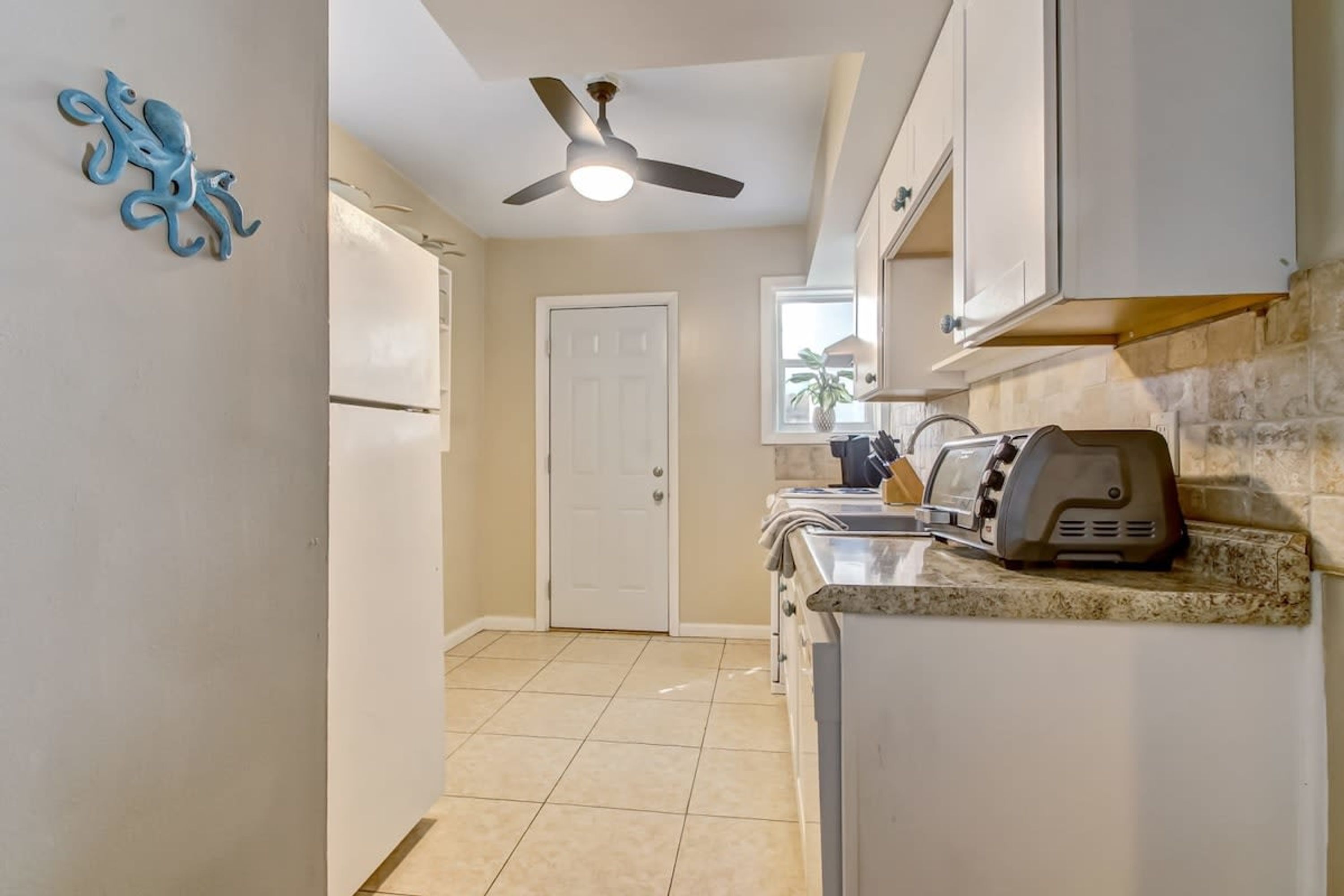 A kitchen with white cabinets, a ceiling fan, a toaster, and a door leading to another room.
