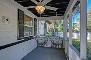A covered porch with two metal chairs, a ceiling fan, and a number '9' sign on the wall.