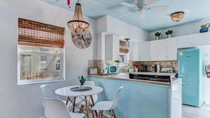 Une cuisine moderne avec un îlot central bleu, des armoires blanches et un ventilateur de plafond.