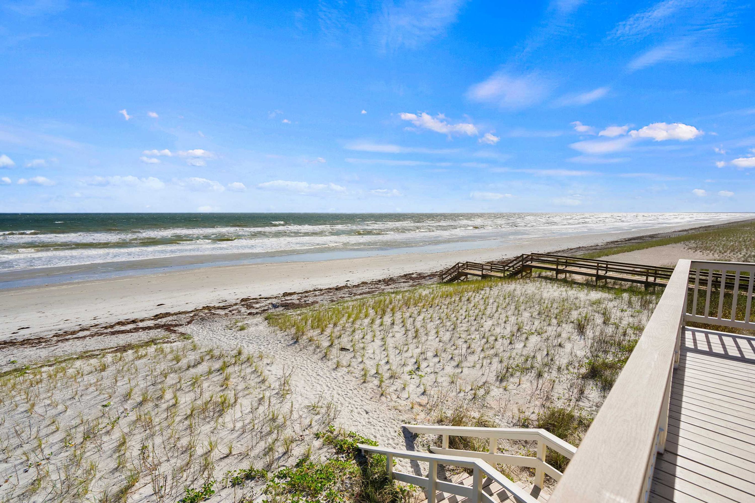 A beach with a wooden boardwalk leading to the shore, sandy dunes, and the ocean.