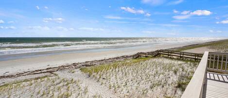 A beach with a wooden boardwalk leading to the shore, sandy dunes, and the ocean.