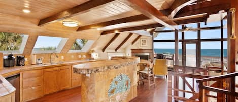 A spacious kitchen with wooden beams, a large island, and a view of the ocean.