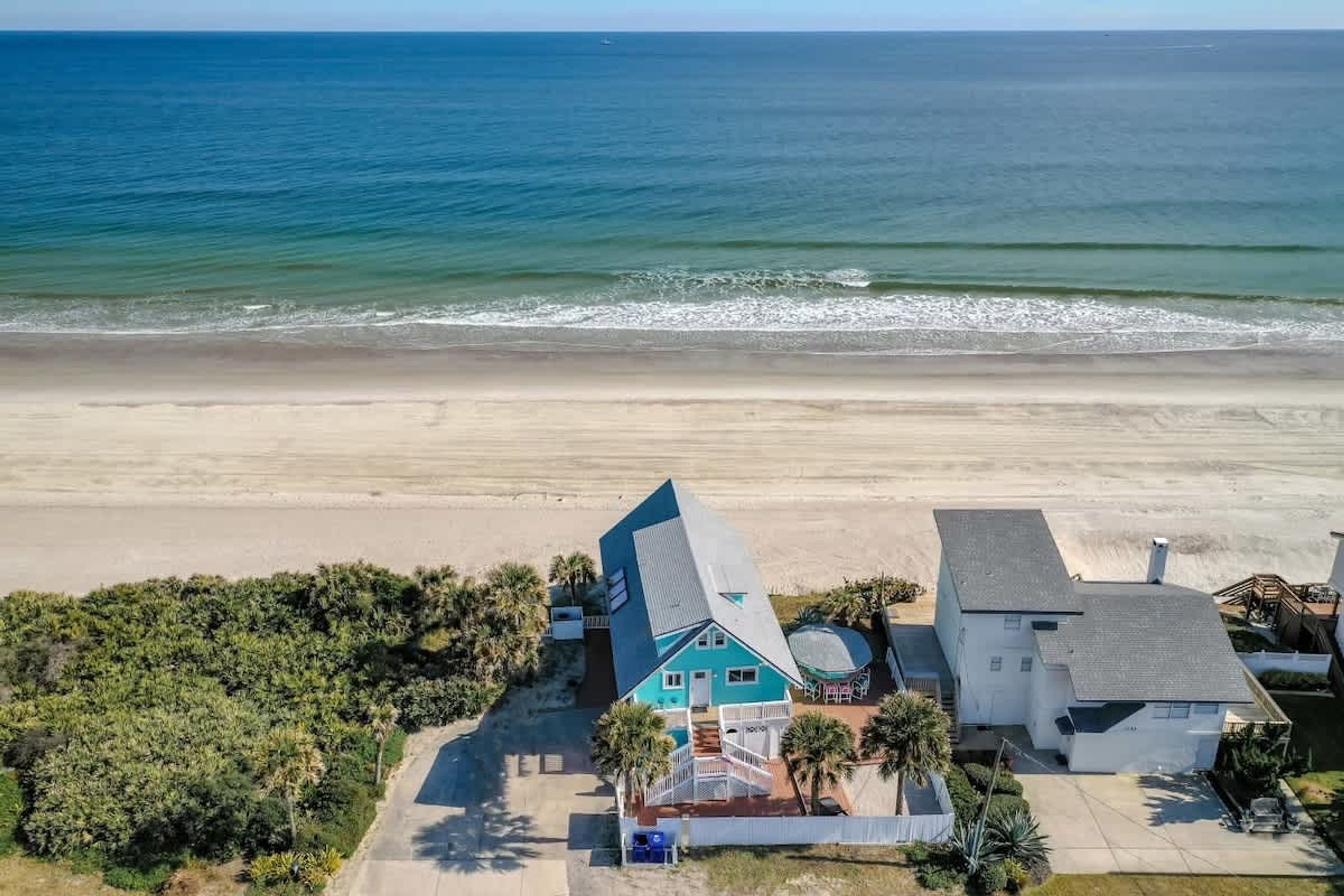 Une propriété située sur la côte, comprenant une grande maison et un bâtiment plus petit, le tout entouré d’une plage et d’une végétation luxuriante.