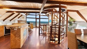 Amplia habitación con techo de madera, una escalera en espiral central y vista al océano.