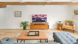 Un salon moderne avec un meuble TV en bois, une grande peinture représentant un coucher de soleil, un canapé, une table basse et une table d’appoint avec une plante.