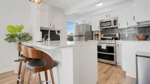 Une cuisine moderne avec des meubles blancs, des appareils en acier inoxydable et un îlot central doté de tabourets de bar.