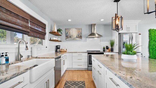 A modern kitchen with white cabinets, a granite countertop, a stainless steel range hood, and a built-in refrigerator.