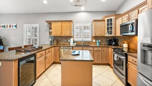 A spacious kitchen with granite countertops, wooden cabinets, a central island, stainless steel appliances, and a large window with blinds. - Pool Hot Tub Dock Walk to Beach Beach Gear (St. Augustine)