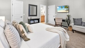 A bedroom with a large bed, a desk, a chair, a TV, and a painting of a beach. - Pool Hot Tub Dock Walk to Beach Beach Gear (St. Augustine)