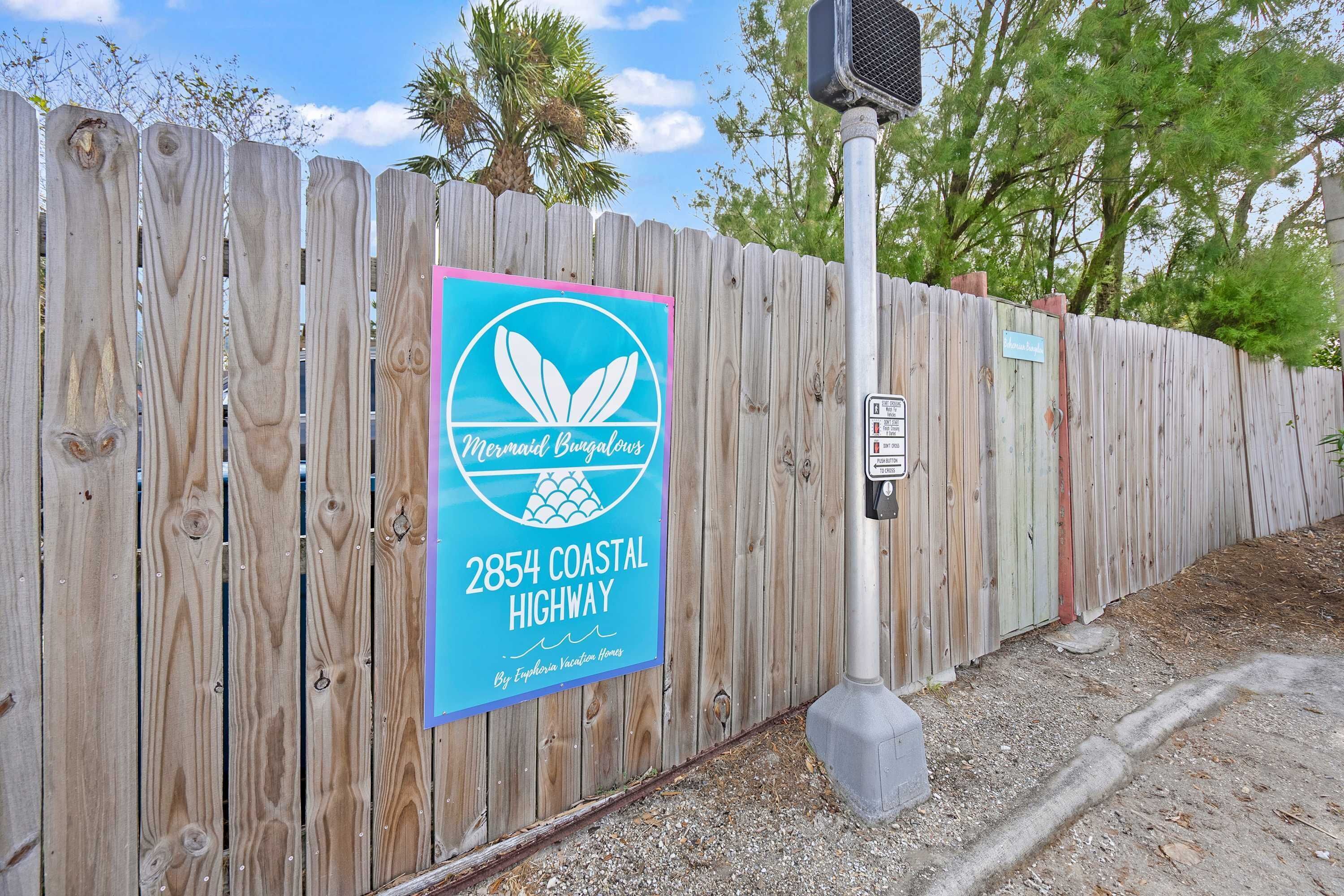 A wooden fence with a sign indicating "Mermaid's Beachfront" at 2854 Coastal Highway.